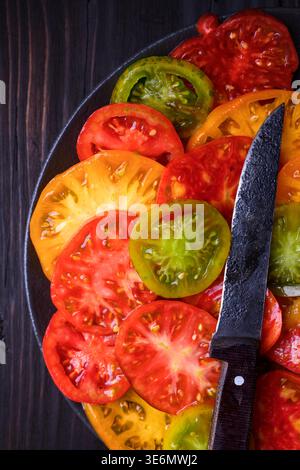 Overhead view of sliced tomatoes on dark wooden surface with knife. Natural seasonal vegetables, healthy cooking concept Stock Photo