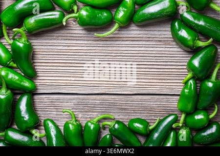 Frame made of jalapeno peppers on wooden background with empty center. Fresh green chili border composition copy space Stock Photo