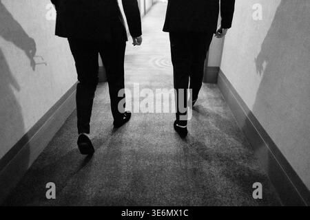 Two Persons Moving Through Corridor With Formal Attire And Dramatic Lighting Stock Photo