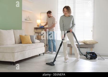 Woman vacuuming and man wiping dust at home, selective focus Stock Photo