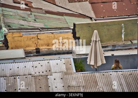 Urban Rooftop Scene With Corrugated Metal Roofs, A Closed Patio Umbrella And A Person In Valparaiso, Chile. Stock Photo