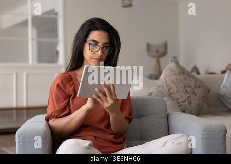 Woman holding tablet seated on cozy armchair in living room Stock Photo