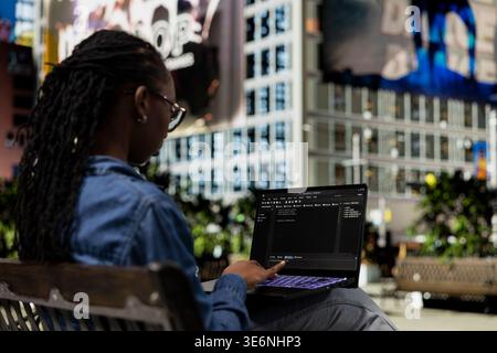 Software developer on park bench writes code on laptop, implementing algorithms. Female programmer using programming languages script program on notebook display, freelancing outdoors Stock Photo