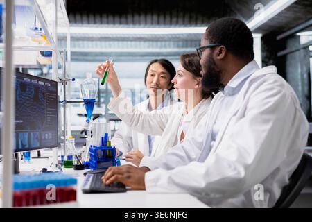 Multiethnic lab technicians inspect liquids in test tube, looking for breakthroughs during clinical trials. Diverse team of research facility staff members comparing chemicals vials, testing formula Stock Photo