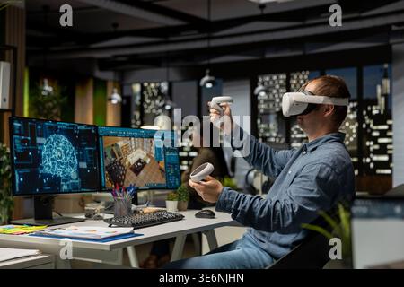Male engineer using VR headset and AI on interior design software at workstation, moving assets for apartment layout with artificial intelligence suggestions in 3D render program. Stock Photo