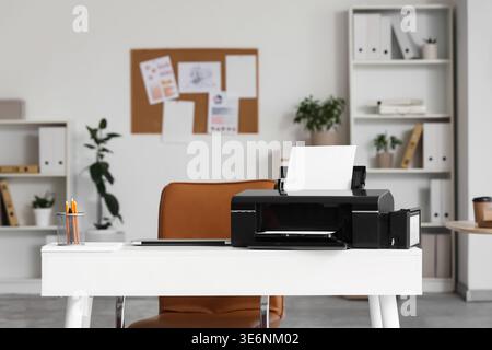 Modern printer with paper sheets and laptop on desk in office Stock Photo