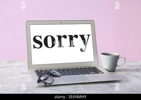 Laptop with word SORRY on grey grunge table Stock Photo
