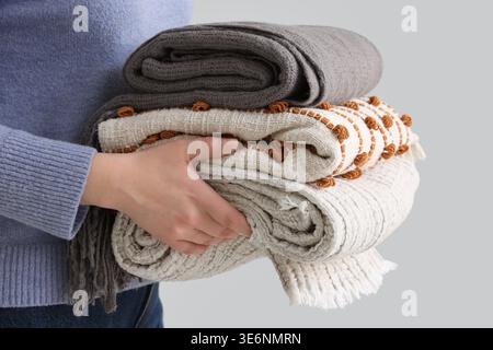 Woman with stack of plaids on light background, closeup Stock Photo