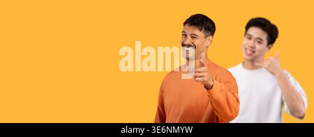 Friendly Man in Orange Sweater Points at Camera With a Funny Smile on Bright Orange Background Stock Photo