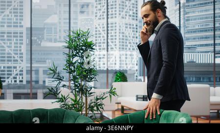 CEO multitasking and managing an important phone call with investors while he reviews financial reports on his laptop. Strategic decision making in corporate life at the workplace. Camera B. Stock Photo