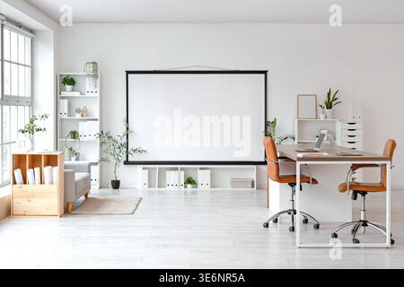 Interior of modern conference hall with laptops on table and projector screen in light office Stock Photo