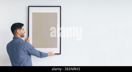 Man Holds Picture Frame on Wall While Preparing for Artwork Placement in a Modern Space Stock Photo