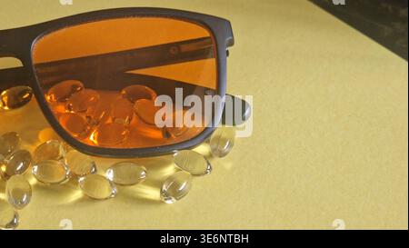 Blue light blocking glasses and omega-3 softgel capsules on a yellow background for health Stock Photo