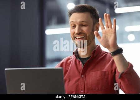 Man Waves During Online Meeting at a Modern Office Space in the Afternoon Stock Photo