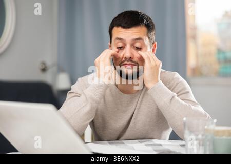Young man rubbing tired eyes while working on computer at home Stock Photo