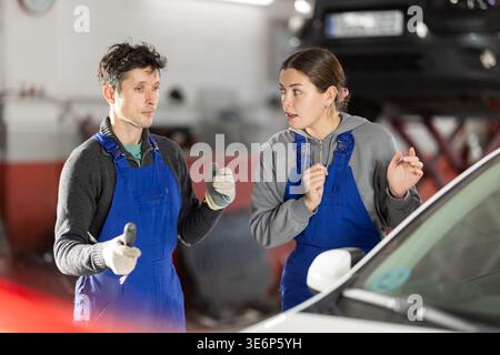 Two auto mechanics, man and woman, diagnosing a car engine together in car repair shop Stock Photo