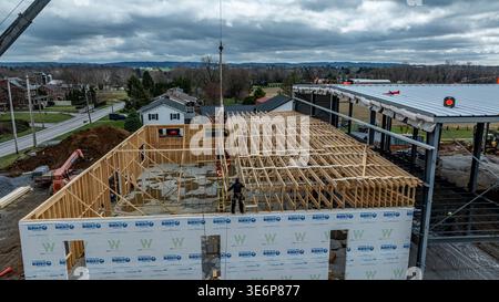 A construction crew works on the wooden frame of a new building in a suburban location. The scene shows workers using cranes and equipment. Clouds fill the sky above. Stock Photo