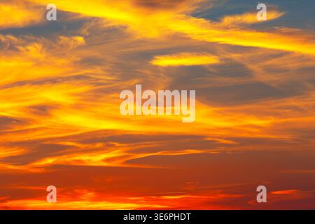 Clouds streak across the sky as the twilight, painting the horizon in shades of orange, red, and gold. Scene glows warmly, blending light and color in Stock Photo