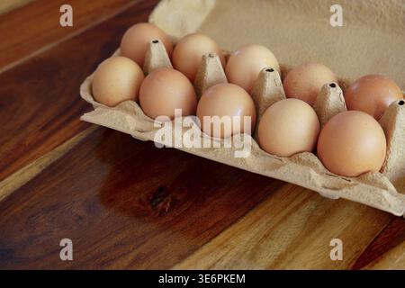 Brown chicken eggs neatly arranged in an open recyclable cardboard carton on a warm polished wooden surface, overhead view with ample copy space for f Stock Photo