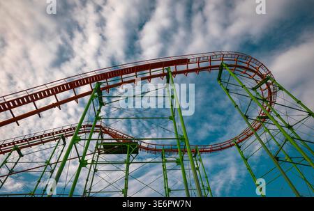 Intricate green steel support beams and orange tracks viewed from below against a cloudy sky Stock Photo