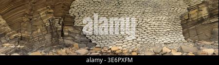 Sedimentary coastal cliffs protected by a stacked sandbag revetment installed to slow erosion from waves undercutting the base. The rounded shapes in Stock Photo