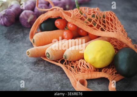 Fresh vegetables and fruits in an orange mesh bag on a table Stock Photo
