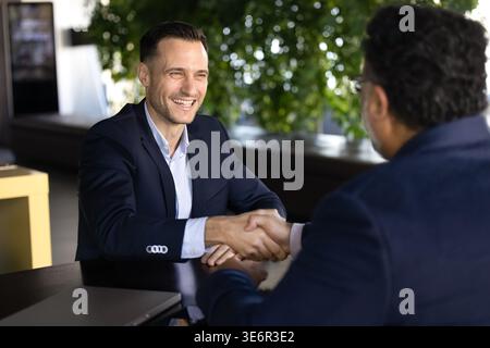 Two businessmen or applicant and HR manager handshaking sitting at office table, building professional relationships, expressing respect, closing comm Stock Photo