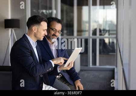 Two businessmen professional, male colleagues reviewing digital data on tablet during strategy meeting, project detail discussion in corporate office. Stock Photo
