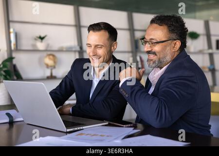 Two businessmen colleagues sit at desk reviewing project result, analyze charts, discuss next steps, engage in positive teamwork, collaborate on busin Stock Photo