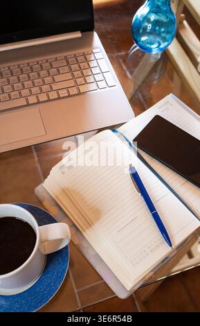 Coffee mug, laptop, and planner on a glass table creating a home office setup Stock Photo