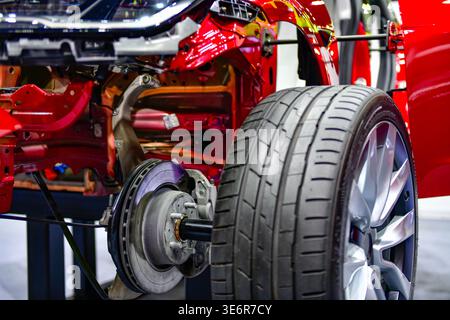 Close-up of a modern vehicle's rear suspension system, featuring disc brakes, calipers, and alloy wheels on a red car chassis display Stock Photo