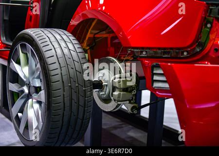 Close-up of a modern vehicle's rear suspension system, featuring disc brakes, calipers, and alloy wheels on a red car chassis display Stock Photo