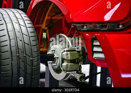 Close-up of a modern vehicle's rear suspension system, featuring disc brakes, calipers, and alloy wheels on a red car chassis display Stock Photo
