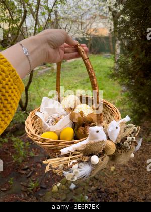Hand holding rustic easter basket with eggs and treats outdoors Stock Photo