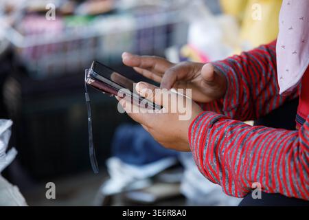 Female vendor's hands using smartphone, daily smartphone activity, modern urban routine, close up. Stock Photo