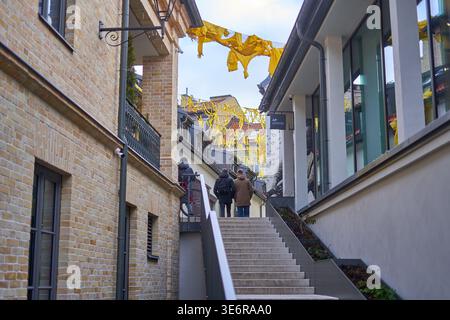 An outdoor urban scene featuring a narrow alleyway with concrete stairs ascending between buildings in Vilnius, Lithuania. On the left is a historic Stock Photo