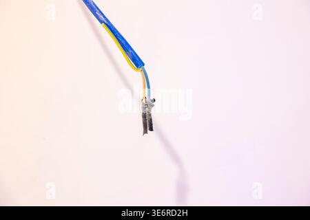 Exposed electrical wires hanging from ceiling in unfinished indoor room, damaged insulation. Concept: electrical hazard Stock Photo