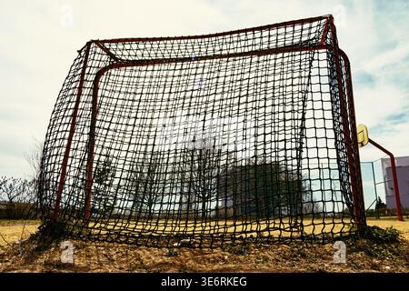 A perspective shot of an orange metal soccer goal with a black net, captured from a side angle on a sandy sports pitch Stock Photo