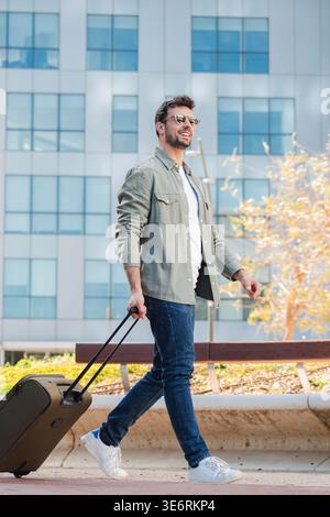 A cheerful man strolling along with a suitcase, eager to embark on his next adventure or travel. His confident demeanor reflects a sense of excitement Stock Photo