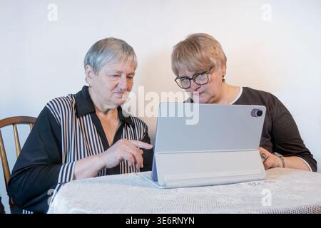 serious elderly pensioner and a middle aged are learning to use tablet on a white background. Stock Photo