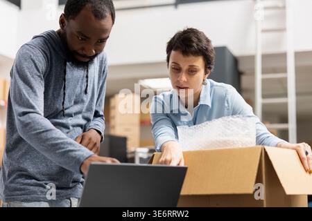 Two diverse employees focusing on logistics and overseeing product handling, working with taped boxes on warehouse shelves. Order fulfillment for a local retail delivery service. Stock Photo