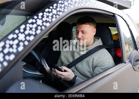 Driver using smartphone while wearing seatbelt in parked car Stock Photo