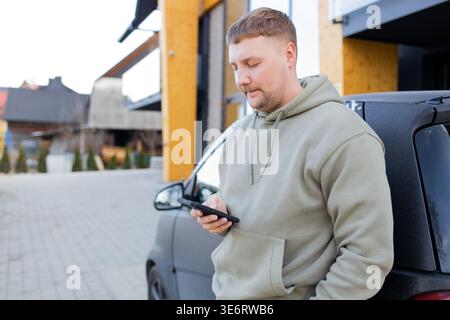 Man using smartphone standing near car outdoors Stock Photo
