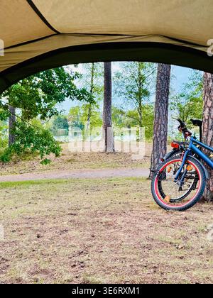 View from inside camping tent to forest and lake with bicycle, camping perspective concept. Stock Photo