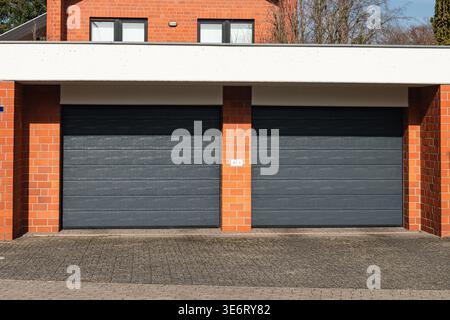 Two closed garage doors are seen at a residential building. The building has red brick walls and a clean driveway. The weather looks nice with clear s Stock Photo