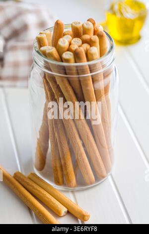 Crunchy Italian breadsticks (grissini) stacked in a clear glass jar on a bright white tabletop, perfect for snacks, antipasto platters or casual enter Stock Photo