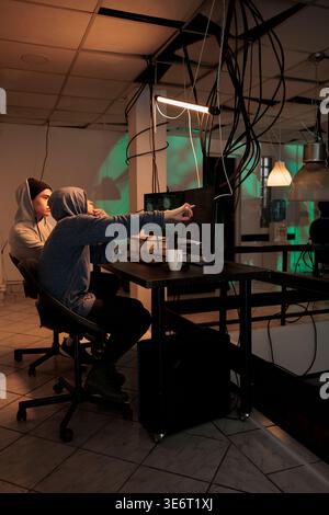 Man and woman hacking professional network to steal sensitive data, using malware for phishing. Team of spies trying to crack encryption, hacking cyberspace with virus. Leak information. Stock Photo