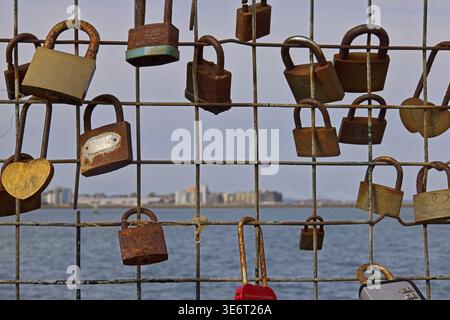 Love locks attached to harbour fence at Newhaven, Edinburgh, with Granton coastline blurred in background Stock Photo