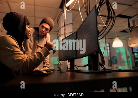 Team of hackers looking at spyware and phishing technology to hack government network. Criminals working on identity theft with malware and virus, planning security breach at night. Stock Photo