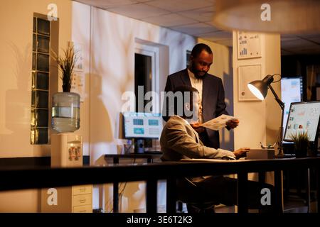 African american businessmen looking on financial reports, checking statistics graphs before start working at marketing strategy. Colleagues discussing company growth report late at night Stock Photo